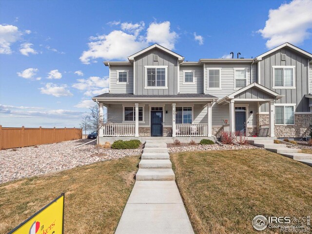 view of front of house with a front yard, stone siding, fence, board and batten siding, and a porch
