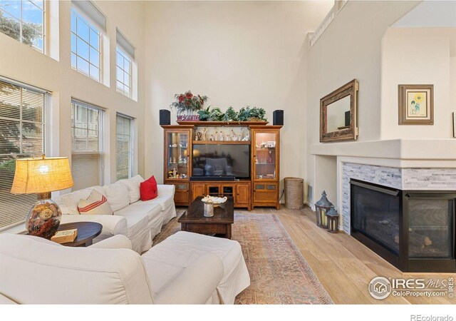 living room with a towering ceiling, a glass covered fireplace, and wood finished floors