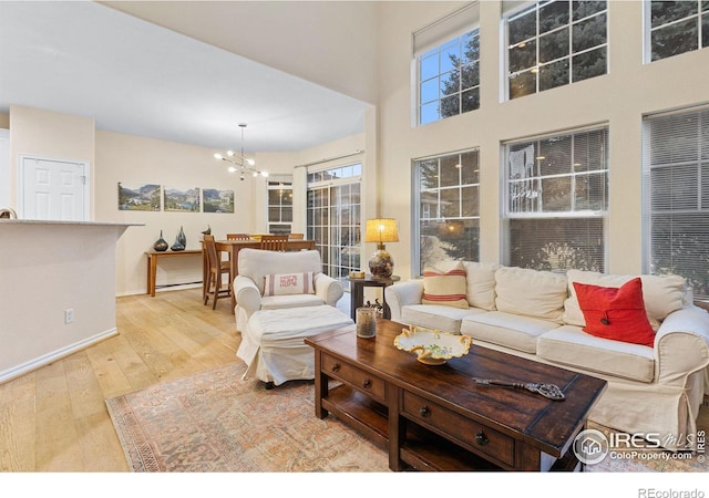 living area featuring baseboards, light wood-style flooring, a towering ceiling, and a chandelier