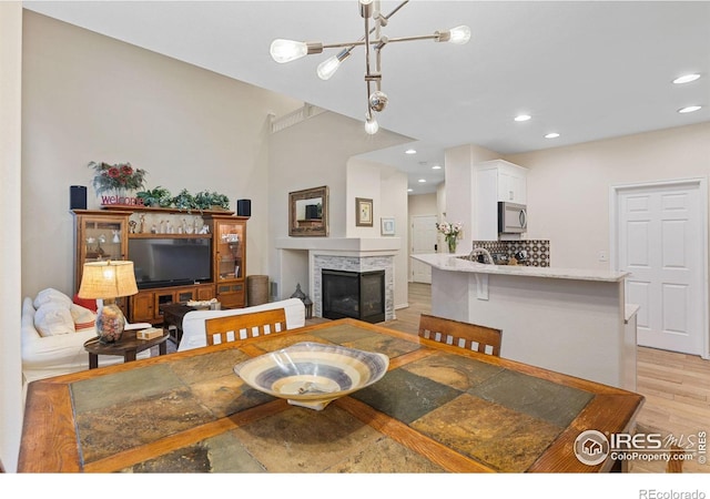 dining space featuring a multi sided fireplace, recessed lighting, a notable chandelier, and light wood-style flooring