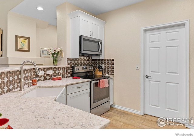 kitchen with light wood-type flooring, white cabinets, tasteful backsplash, a sink, and stainless steel appliances
