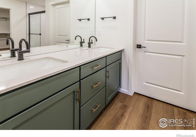 bathroom with double vanity, wood finished floors, a stall shower, and a sink