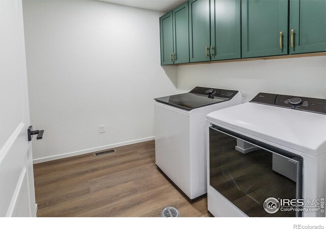 clothes washing area with wood finished floors, visible vents, washing machine and dryer, baseboards, and cabinet space
