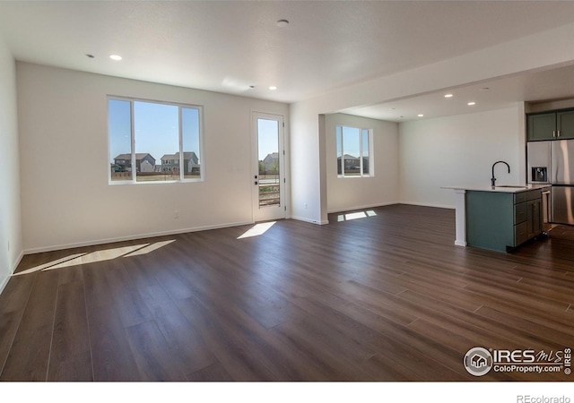 unfurnished living room featuring dark wood-style flooring, a healthy amount of sunlight, and a sink