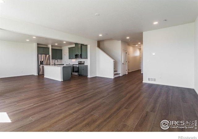 unfurnished living room with dark wood-style floors, baseboards, visible vents, recessed lighting, and stairway
