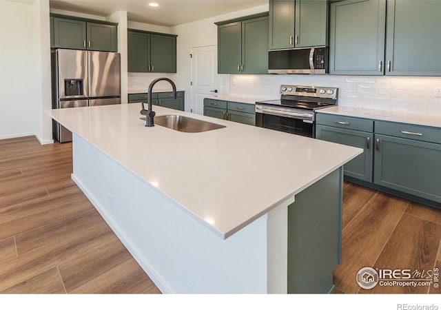 kitchen featuring dark wood-style floors, stainless steel appliances, a sink, green cabinets, and tasteful backsplash