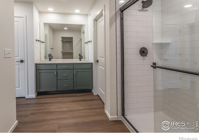 bathroom featuring a tile shower, wood finished floors, a sink, and double vanity
