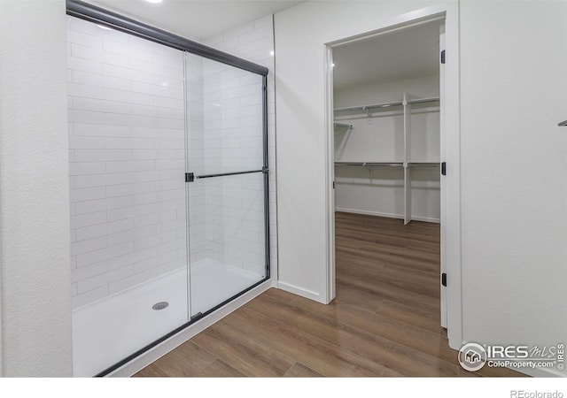 full bath featuring a walk in closet, wood finished floors, baseboards, and a stall shower