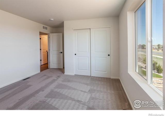 unfurnished bedroom featuring baseboards, a closet, visible vents, and light carpet
