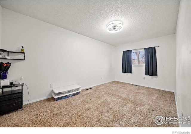 empty room with carpet flooring, visible vents, a textured ceiling, and baseboards