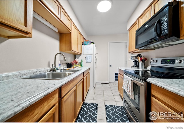 kitchen featuring black microwave, light tile patterned floors, light countertops, stainless steel range with electric stovetop, and a sink