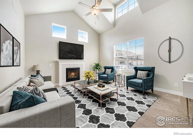 living area with baseboards, a glass covered fireplace, carpet flooring, high vaulted ceiling, and ceiling fan