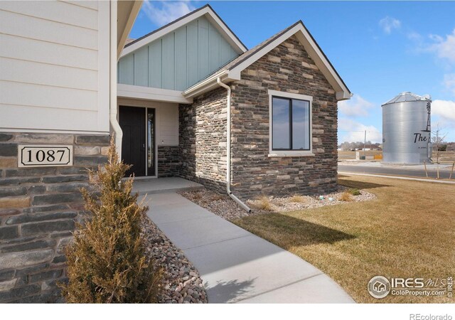 doorway to property with stone siding, board and batten siding, and a yard