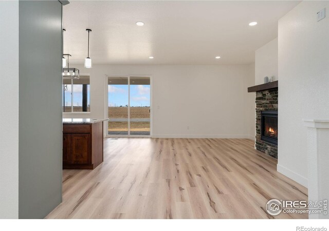 unfurnished living room featuring light wood-style flooring, baseboards, recessed lighting, a stone fireplace, and an inviting chandelier
