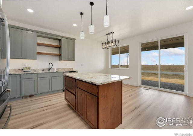 kitchen with a sink, open shelves, light stone countertops, decorative light fixtures, and light wood-style floors