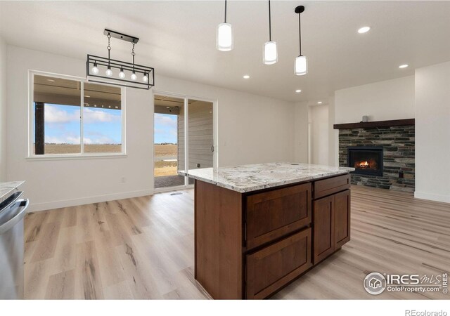 kitchen with light stone counters, pendant lighting, a stone fireplace, open floor plan, and light wood-type flooring