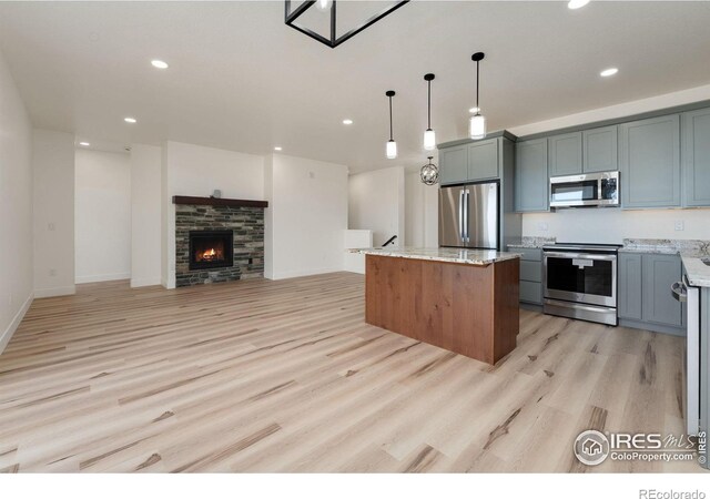 kitchen with light stone counters, a center island, light wood-type flooring, stainless steel appliances, and recessed lighting