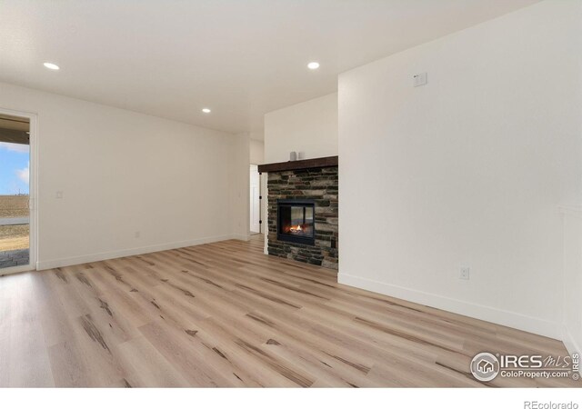 unfurnished living room with light wood finished floors, baseboards, recessed lighting, and a glass covered fireplace