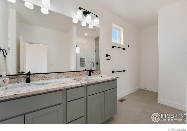 bathroom featuring double vanity, a sink, a stall shower, and baseboards