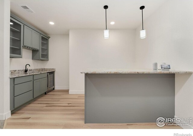 kitchen featuring light wood finished floors, gray cabinetry, glass insert cabinets, visible vents, and decorative light fixtures
