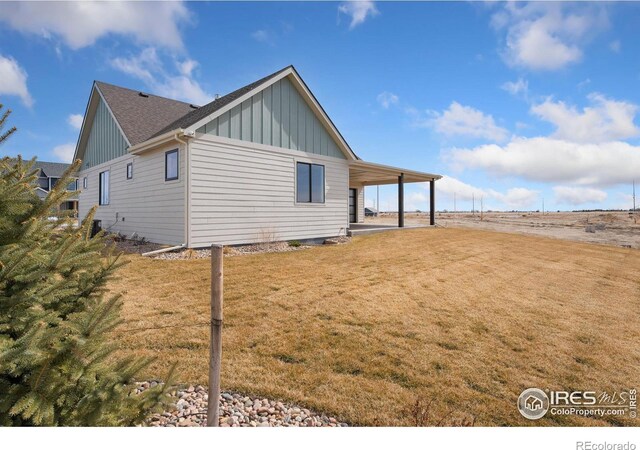 exterior space with board and batten siding, a carport, and a yard