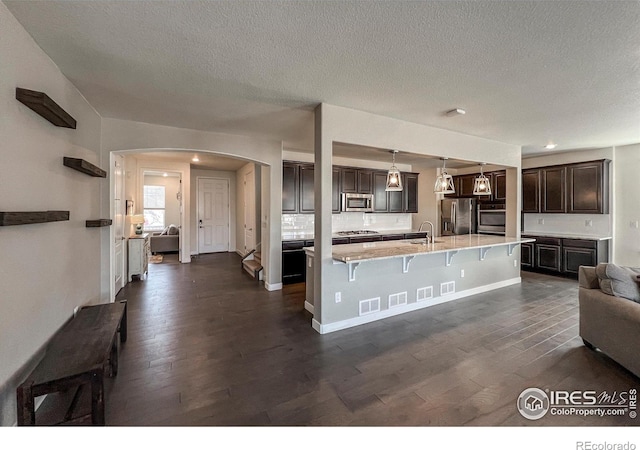 kitchen with appliances with stainless steel finishes, arched walkways, open floor plan, a breakfast bar, and dark brown cabinetry