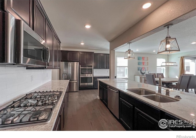 kitchen featuring appliances with stainless steel finishes, a sink, recessed lighting, light stone countertops, and decorative backsplash