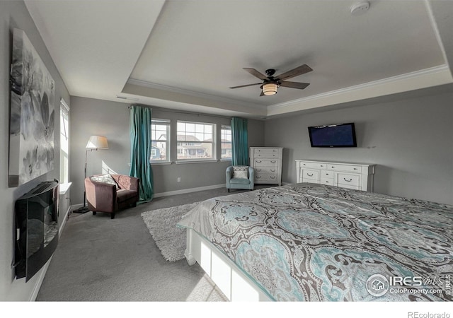 carpeted bedroom featuring a tray ceiling, baseboards, crown molding, and ceiling fan