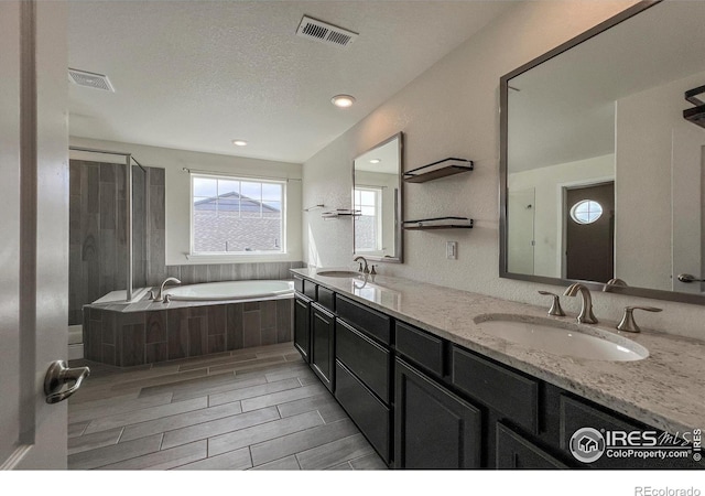 full bath with a bath, double vanity, a shower with shower door, wood tiled floors, and a textured ceiling