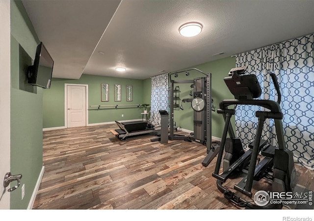 exercise room featuring wood finished floors, baseboards, and a textured ceiling