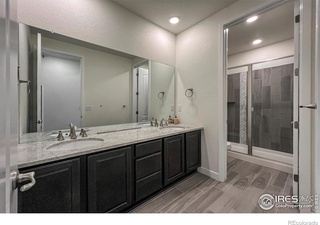 bathroom with a stall shower, toilet, wood finish floors, double vanity, and baseboards