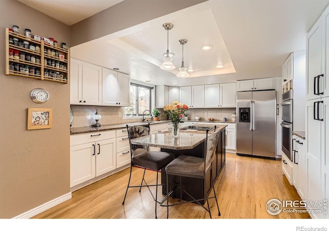 kitchen featuring a tray ceiling, backsplash, light wood-type flooring, and appliances with stainless steel finishes