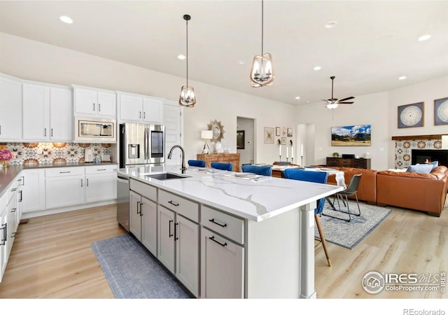 kitchen featuring tasteful backsplash, a sink, light wood-type flooring, appliances with stainless steel finishes, and a ceiling fan