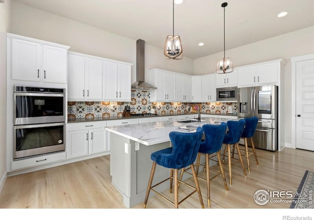 kitchen featuring light wood-style flooring, a sink, wall chimney exhaust hood, and stainless steel appliances