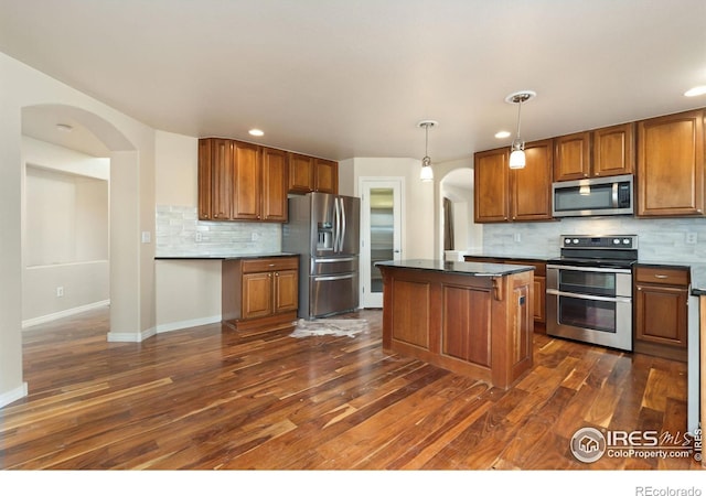 kitchen with backsplash, appliances with stainless steel finishes, dark wood-style floors, brown cabinetry, and arched walkways