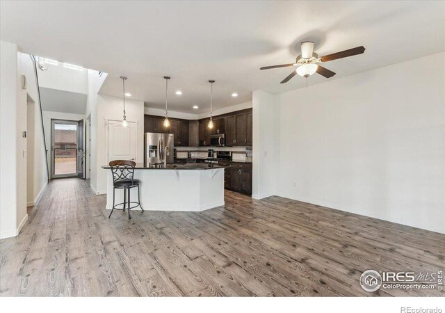 403 S Maple Ave, Eaton, CO 80615 - kitchen featuring appliances with stainless steel finishes, dark brown cabinets, dark countertops, light wood-style floors, and a kitchen bar