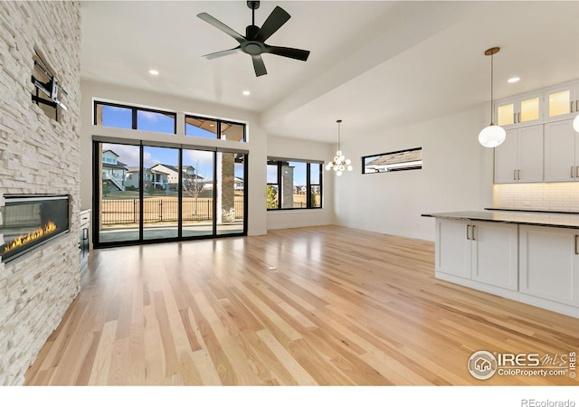 3364 Danzante Bay Ct, Berthoud, CO 80513 - unfurnished living room with a stone fireplace, ceiling fan with notable chandelier, light wood finished floors, and recessed lighting