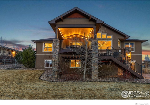 1046 Greens Pl, Erie, CO 80516 - back of property at dusk with stucco siding, stairs, a balcony, and a yard