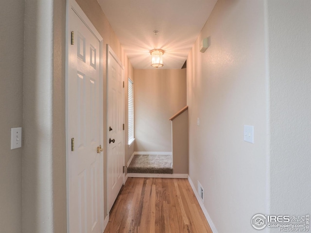 hallway featuring baseboards, light wood-type flooring, visible vents, and stairway
