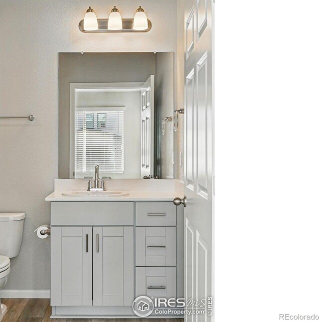 bathroom featuring baseboards, wood finished floors, toilet, and vanity