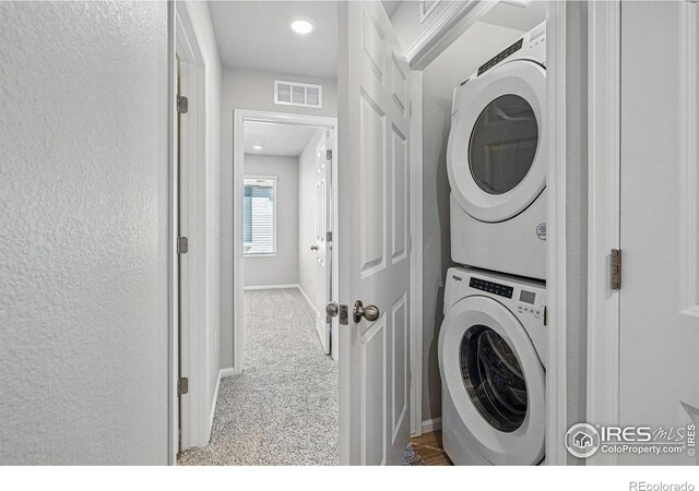 washroom featuring carpet flooring, stacked washer / dryer, laundry area, baseboards, and visible vents