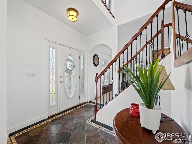 foyer featuring a towering ceiling, arched walkways, baseboards, and stairway