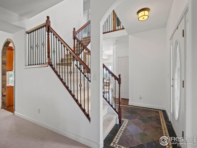 entrance foyer with baseboards, arched walkways, stone finish flooring, and stairway