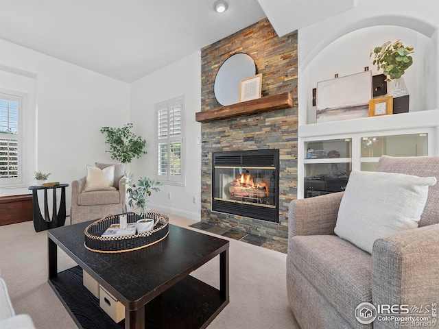 carpeted living area featuring a stone fireplace