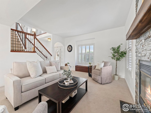 living room with light colored carpet, stairs, baseboards, arched walkways, and a stone fireplace