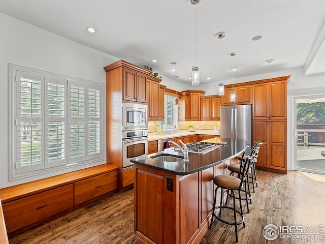 kitchen featuring a kitchen island with sink, brown cabinets, wood finished floors, and appliances with stainless steel finishes