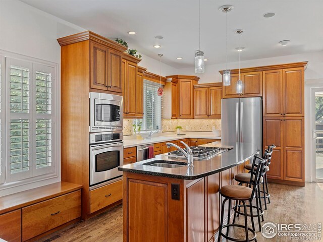 kitchen with an island with sink, a kitchen bar, light wood-type flooring, brown cabinetry, and stainless steel appliances