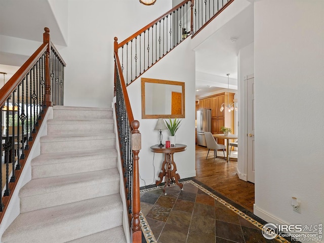 stairway featuring baseboards, a towering ceiling, and stone tile flooring