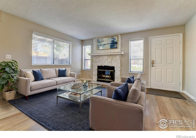 living area featuring a stone fireplace, a wealth of natural light, wood finished floors, and baseboards