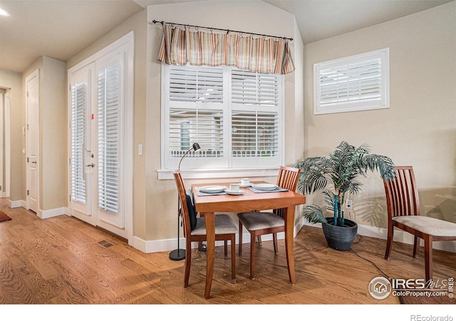 dining room featuring baseboards, visible vents, wood finished floors, and vaulted ceiling